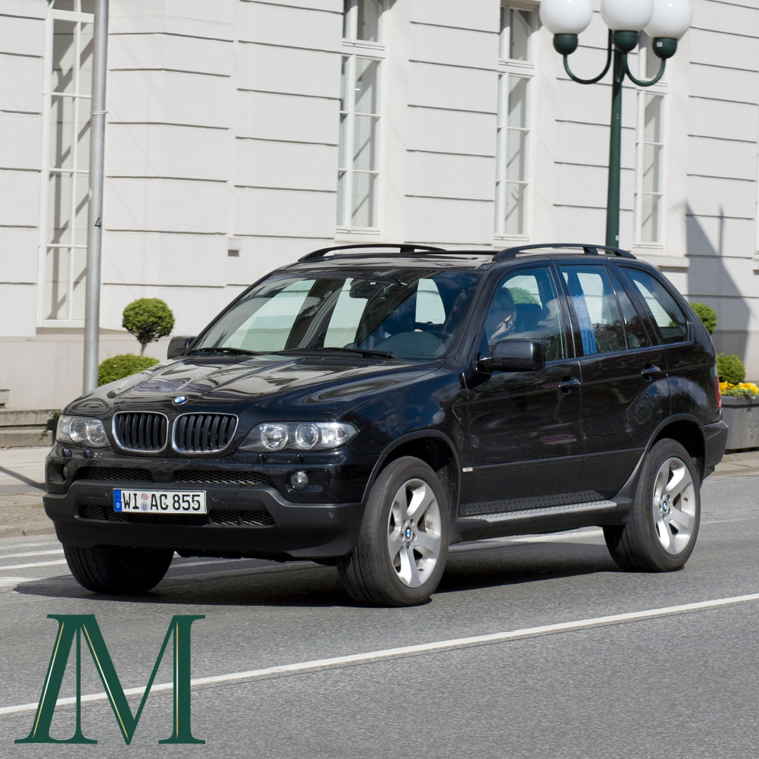 Black BMW X5 SUV driving past a white building, with the Inspired Method logo in the bottom corner