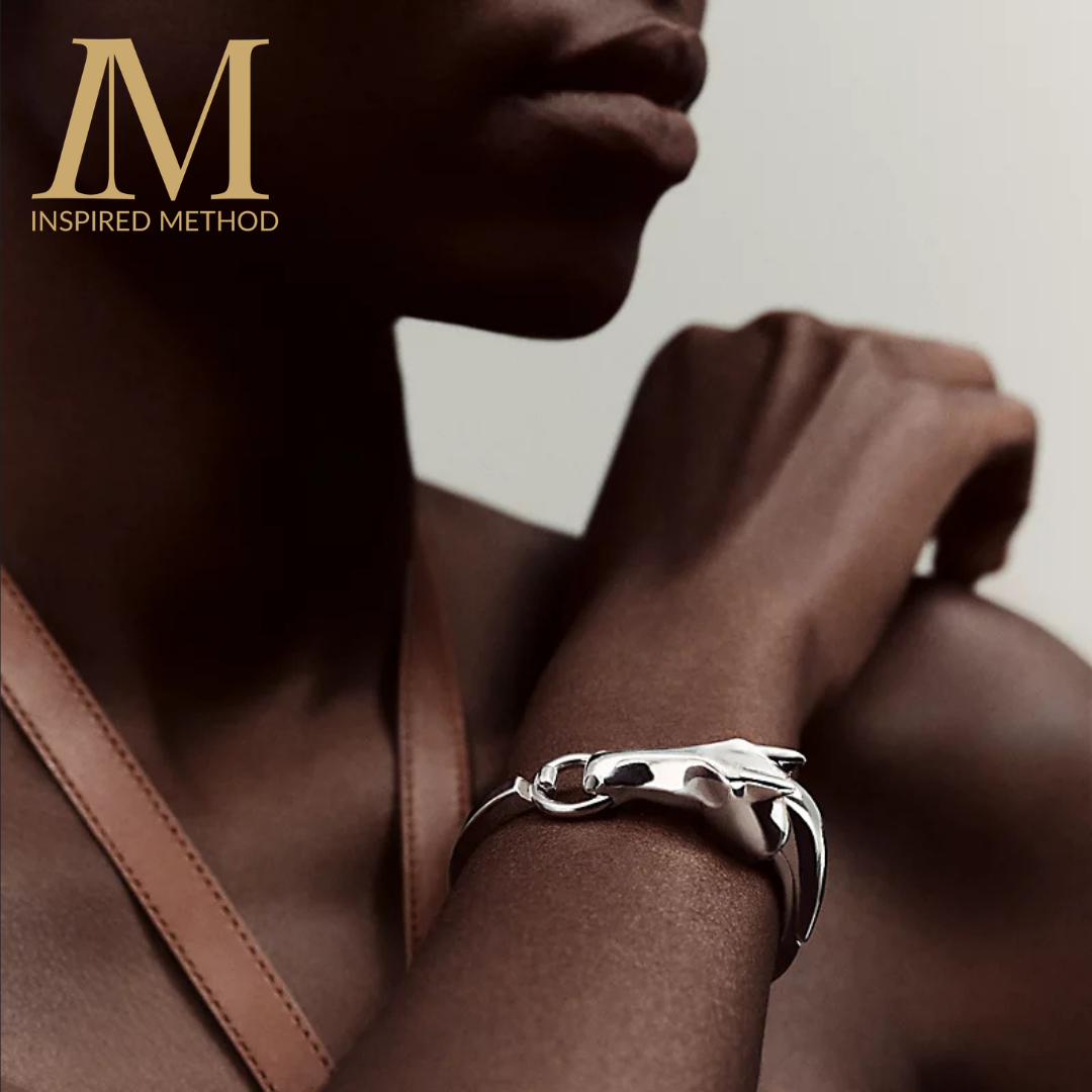 A closeup shot of a person, who's face is cropped, holds up a wrist, wearing an Hermes silver bangle in the shape of a horse.